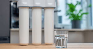 Glass of filtered drinking water and water filtration system on kitchen table